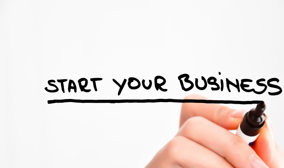 A hand holding a marker is writing the phrase Start Your Business on a clear surface.