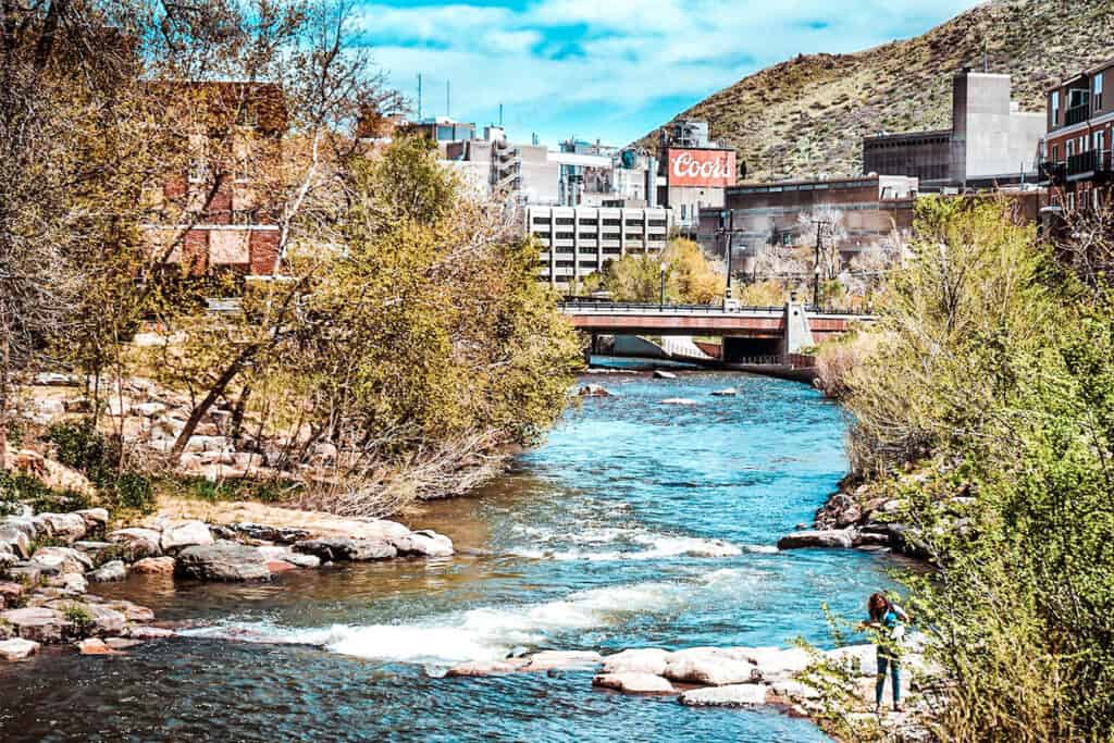 A vibrant photo of a river flowing through an urban area with buildings and a large Cool sign in the background.