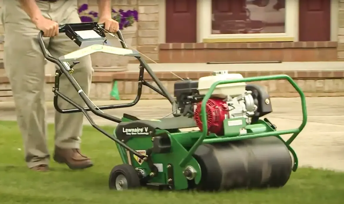 A person is using a walk-behind lawn aerator machine on a grassy lawn.